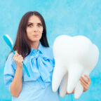 Funny Woman Holding Oversized Tooth in Dentist Concept Image. Cute girl with big wisdom molar or implant mock-up model